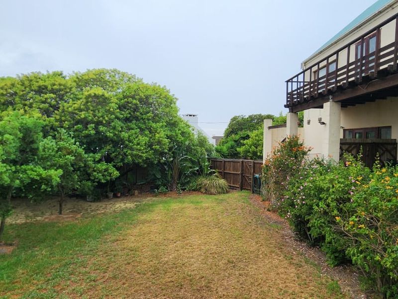 Rear view of the property featuring a lawned garden, established trees, and a wooden balcony extending from the upper level.