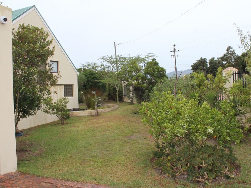 A view of the rear garden area featuring a landscaped lawn, established shrubs, a brick driveway, and a security camera mounted on the building exterior.
