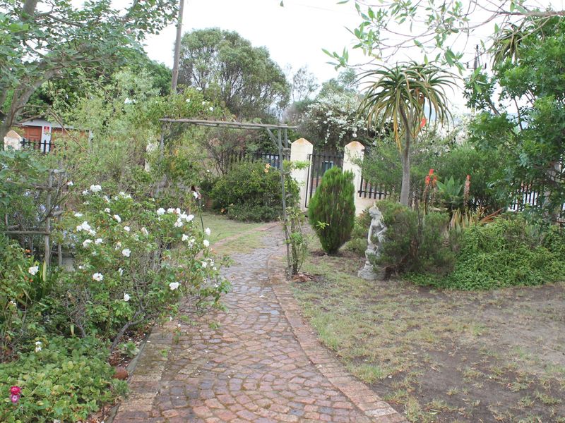 A lush, established garden featuring a cobblestone pathway, mature trees, and secure perimeter fencing with brick pillars.