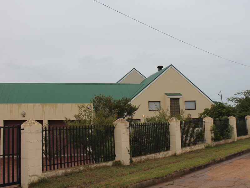 Front view of a house featuring a green metal roof, triple garage, and a perimeter fence with masonry pillars.