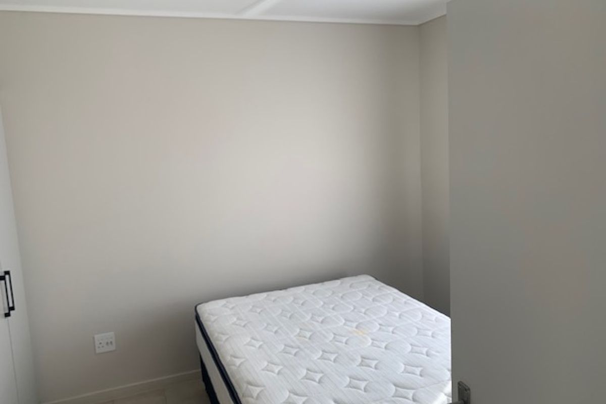 A clean, neutral-toned bedroom featuring a ceiling fan and built-in storage, providing a simple and functional living space.