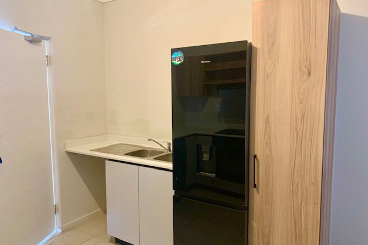 A compact kitchen area featuring white cabinetry, a stainless steel sink, and a tall wood-grain pantry cupboard.