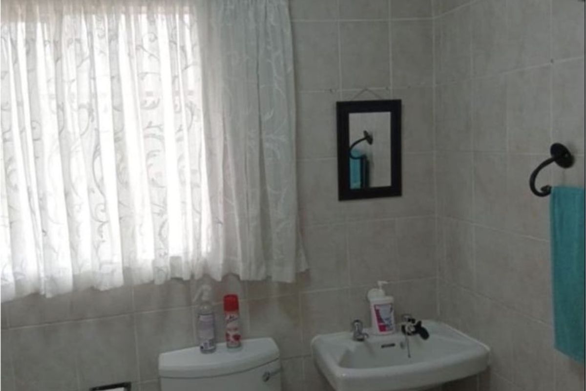 A functional bathroom featuring a pedestal basin, toilet, and neutral ceramic wall tiling.