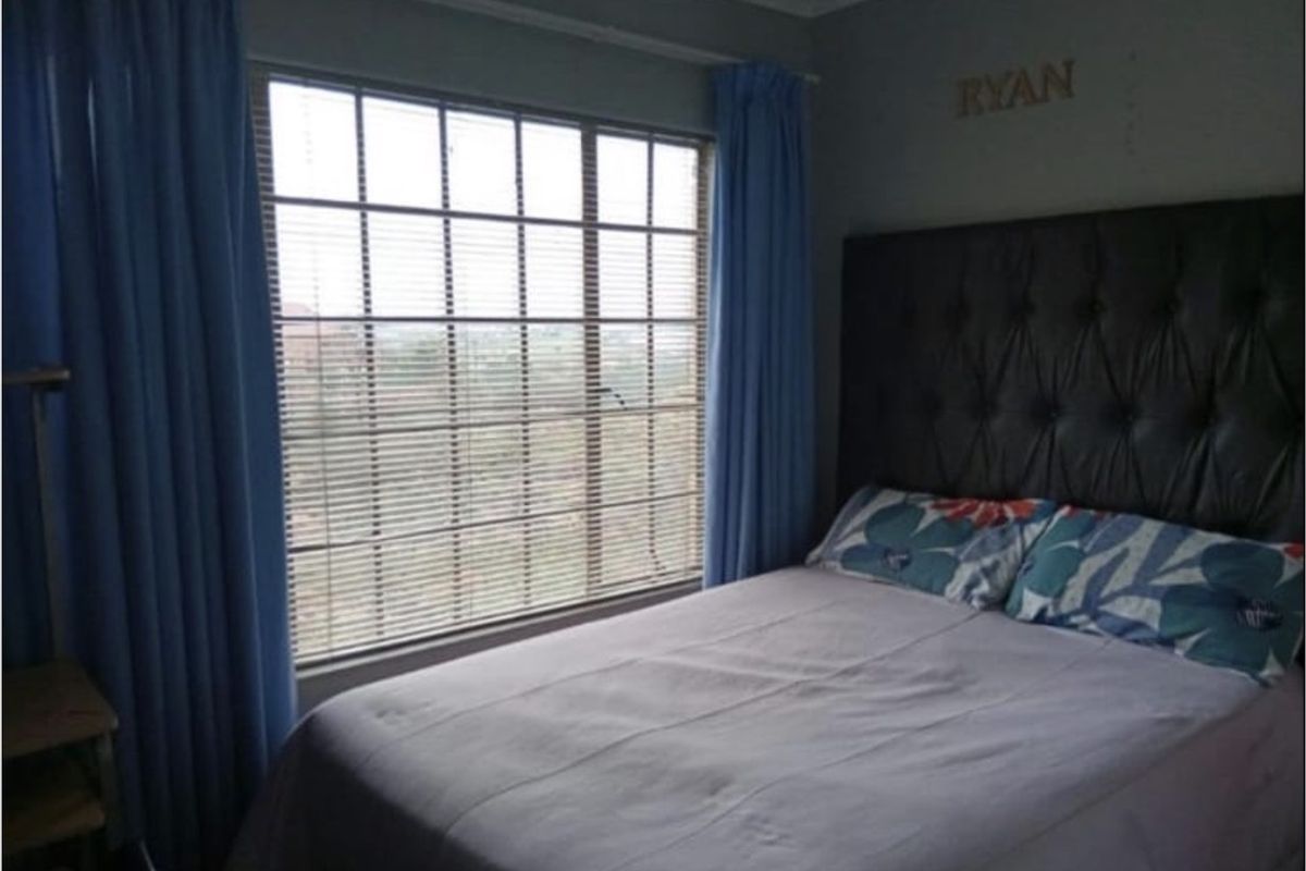 A standard bedroom featuring a large grid-pattern window with venetian blinds and curtain tracks.