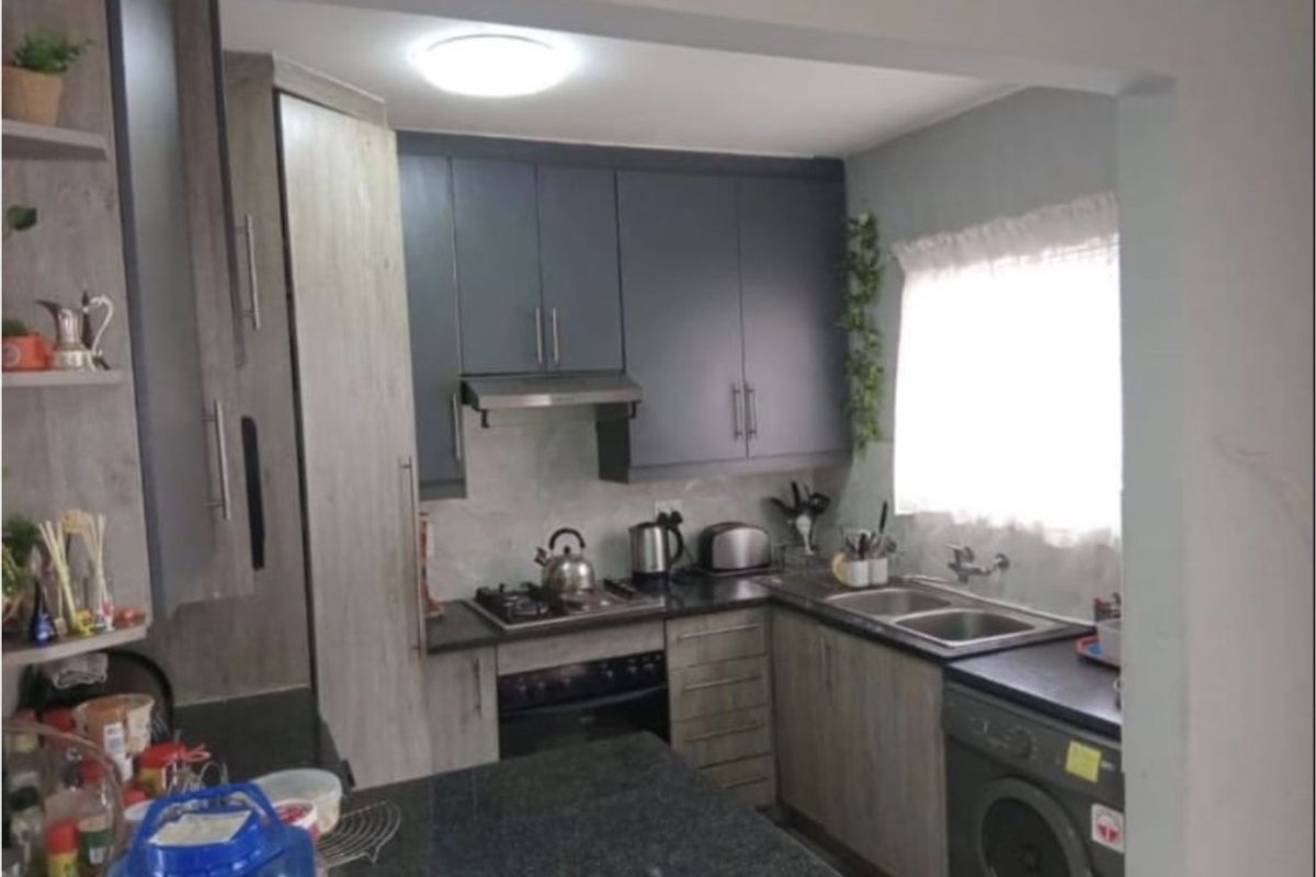Compact kitchen featuring modern dark and wood-grain cabinetry, granite countertops, a gas hob, extractor fan, and integrated laundry plumbing.