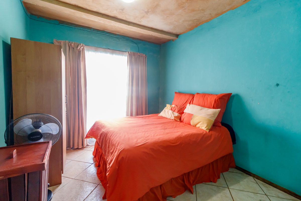 A bedroom featuring tiled flooring and an exposed beam ceiling, currently requiring cosmetic updates to the wall and ceiling finishes.