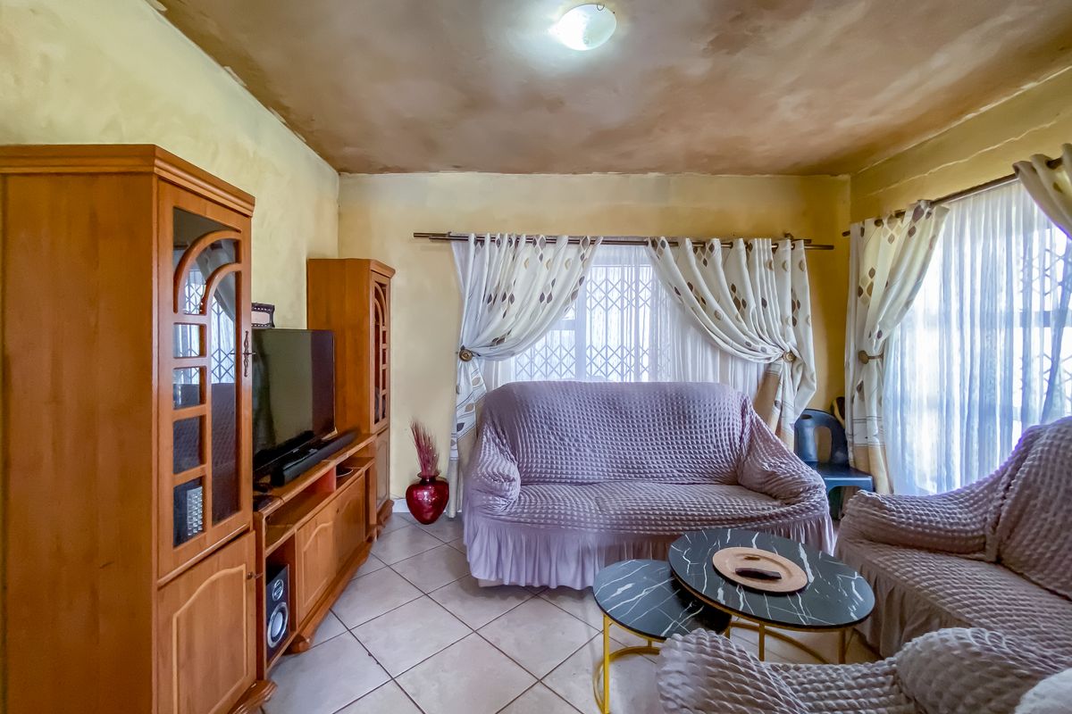 A living room featuring tiled flooring and security gates on the windows, with visible ceiling staining requiring maintenance or cosmetic repair.