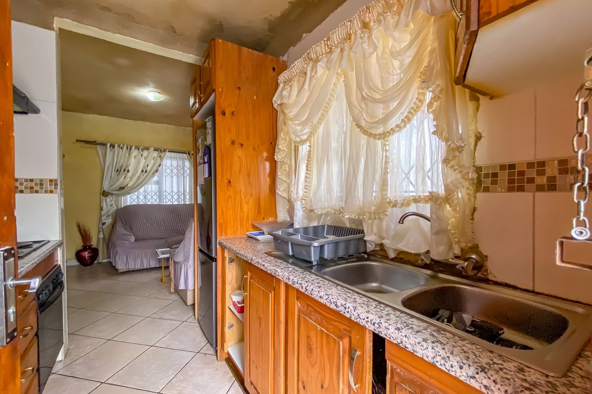 A dated kitchen featuring wooden cabinetry, laminate countertops, and a double bowl sink, requiring significant cosmetic updates and ceiling repairs.