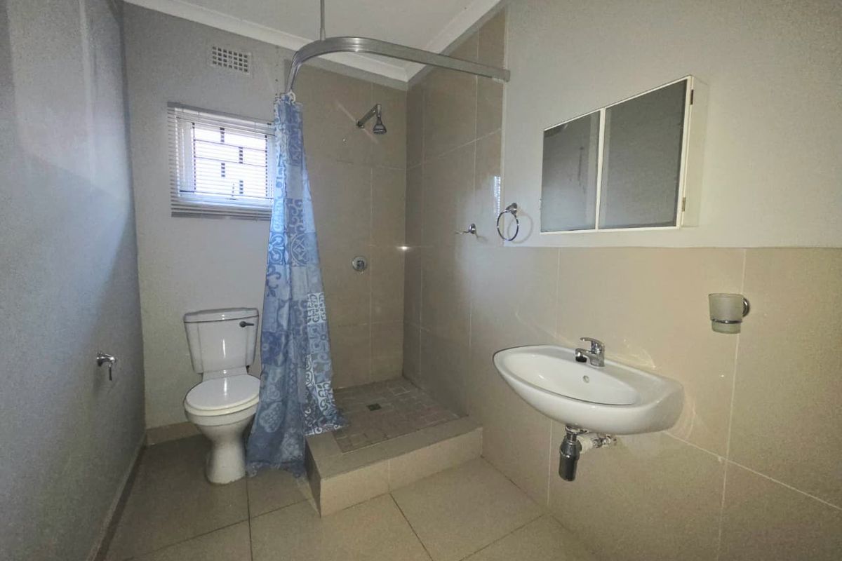 A functional bathroom featuring a walk-in shower, wall-mounted basin, and toilet, finished with neutral wall and floor tiles.