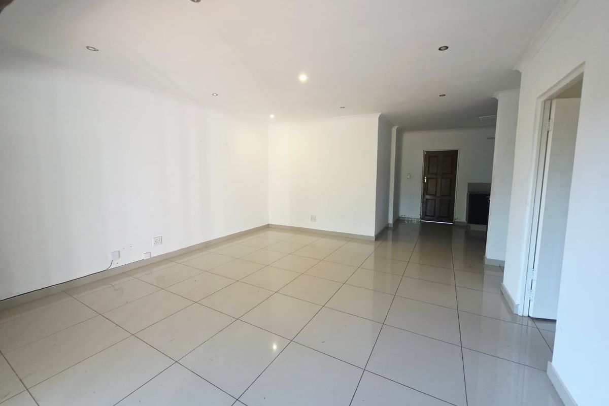 A spacious, empty living area featuring neutral tiled flooring, recessed downlighting, and coved cornicing, providing a blank canvas for interior design.