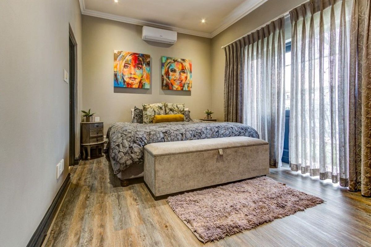 A well-maintained bedroom featuring laminate wood flooring, recessed downlighting, a split-system air conditioner, and direct access to an outdoor area via sliding glass doors.