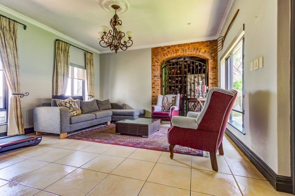 Spacious living room featuring ceramic floor tiles, a decorative ceiling rose with chandelier, and a unique exposed brick archway with a wrought iron gate.