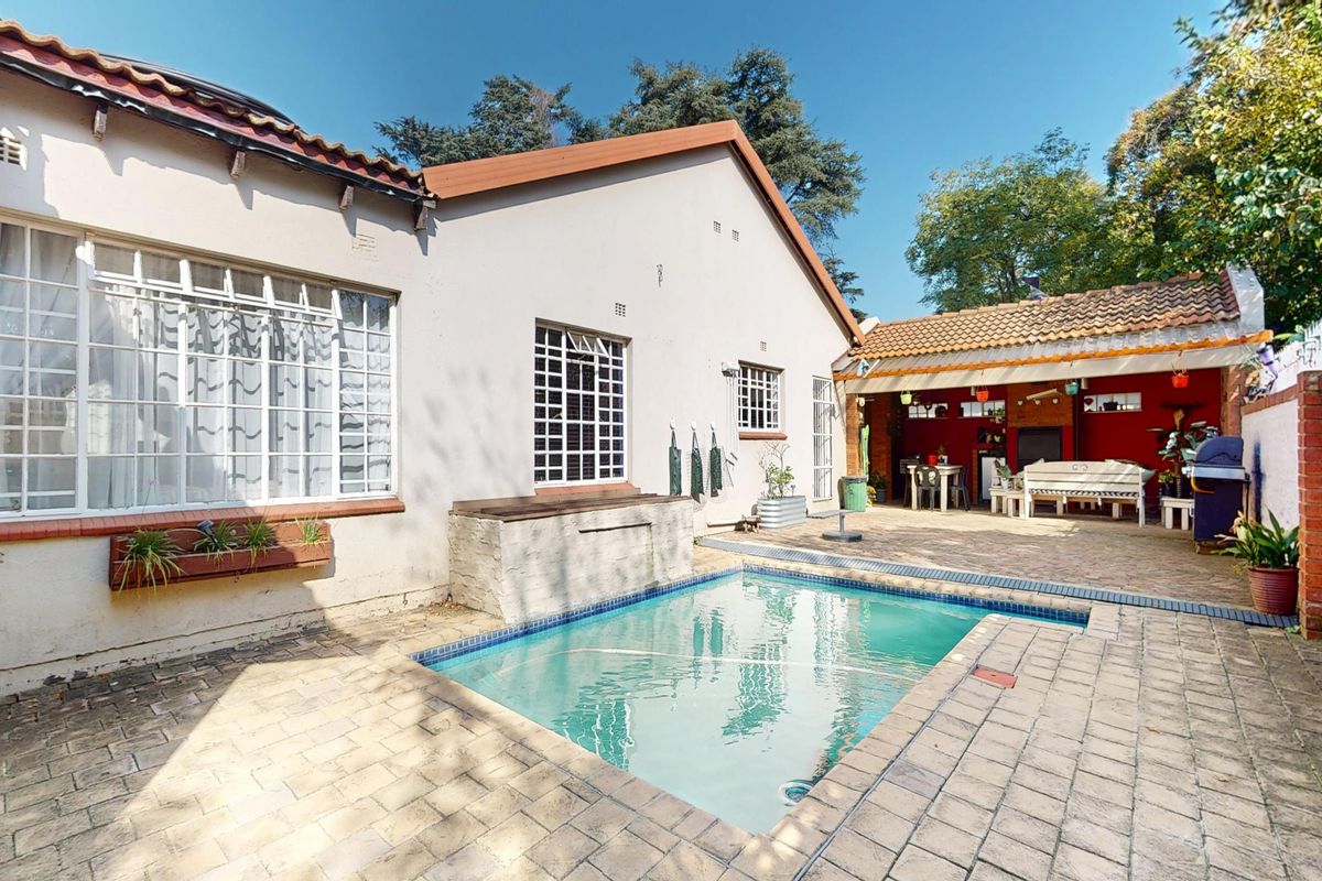 Rear exterior view featuring a swimming pool, paved patio area, and a covered outdoor entertainment space with a brick boundary wall.