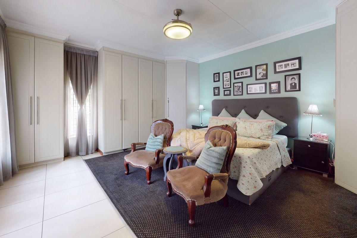 Spacious bedroom featuring extensive built-in cupboards, neutral tiled and carpeted flooring, and a ceiling fan, offering a comfortable and well-maintained living space.