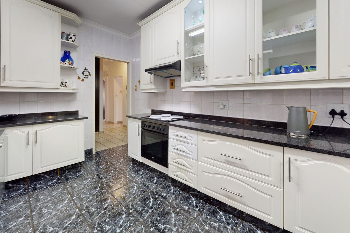 A functional kitchen featuring white cabinetry, dark granite countertops, integrated oven and hob, and marble-effect floor tiles.