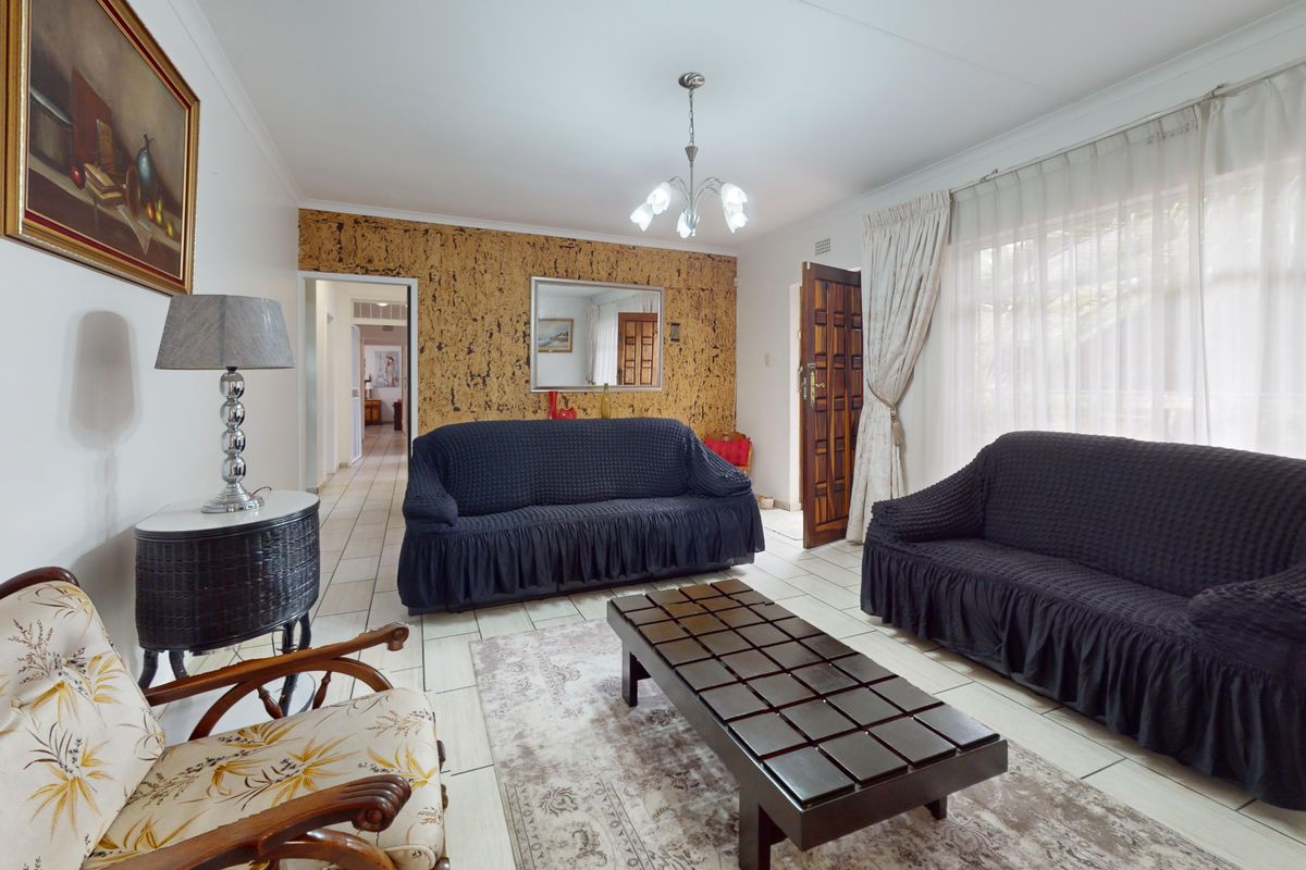 A spacious living room featuring tiled flooring, a distinctive cork feature wall, and natural light through large windows.