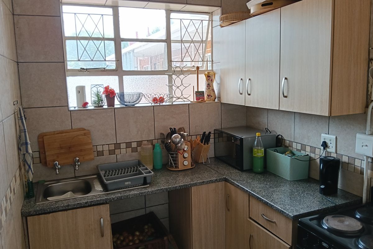 A functional kitchen featuring laminate cabinetry, granite-look countertops, a stainless steel sink, and a tiled backsplash with an integrated electric stove.