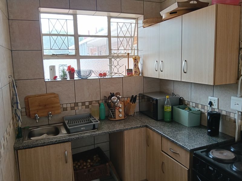 A functional kitchen featuring laminate cabinetry, granite-look countertops, a stainless steel sink, and a tiled backsplash with an integrated electric stove.