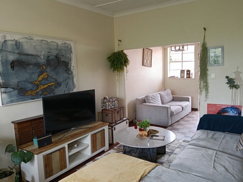 A living room area featuring a connected secondary space, neutral wall finishes, and a multi-pane window providing natural light.