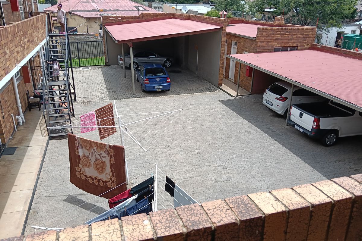 An elevated view of a paved courtyard area featuring covered parking bays and an external metal staircase providing access to the apartment units.