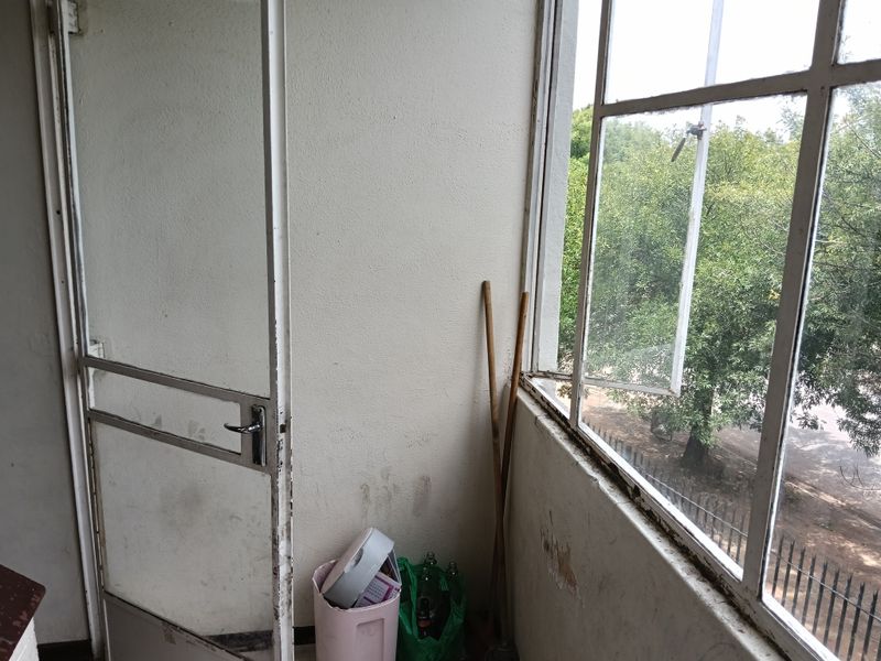 A small balcony area featuring metal-framed windows and a metal door, requiring maintenance and cosmetic updates to improve its overall condition.