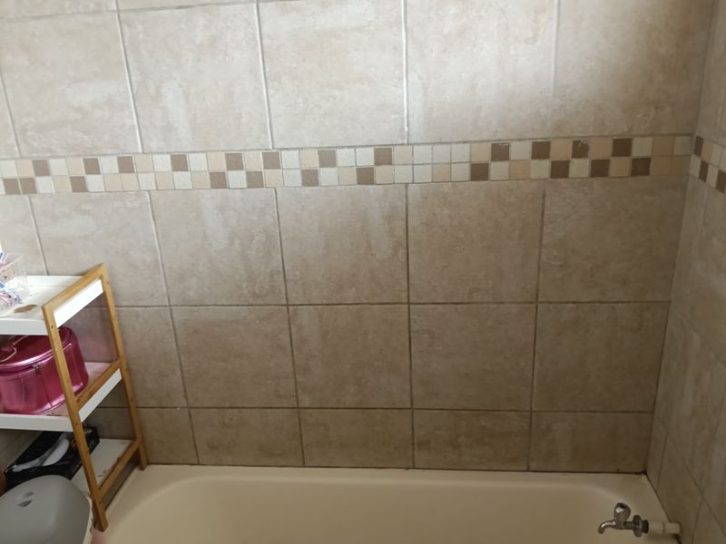 A bathroom area featuring neutral-toned wall tiles with a decorative mosaic border and a standard bathtub with a fitted faucet.