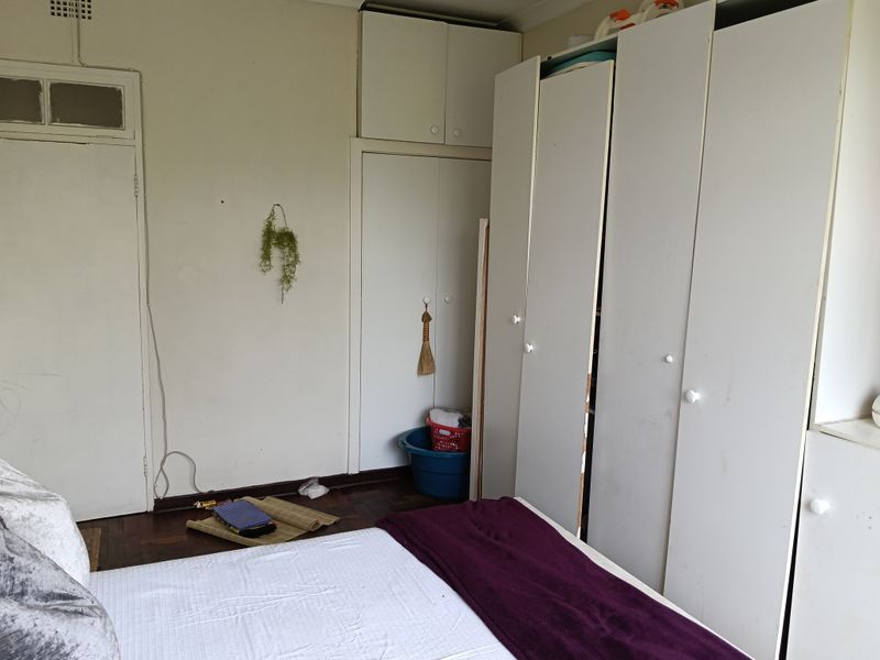 Bedroom featuring parquet flooring and extensive built-in cupboard storage with overhead cabinets, offering a functional layout in need of cosmetic updates.