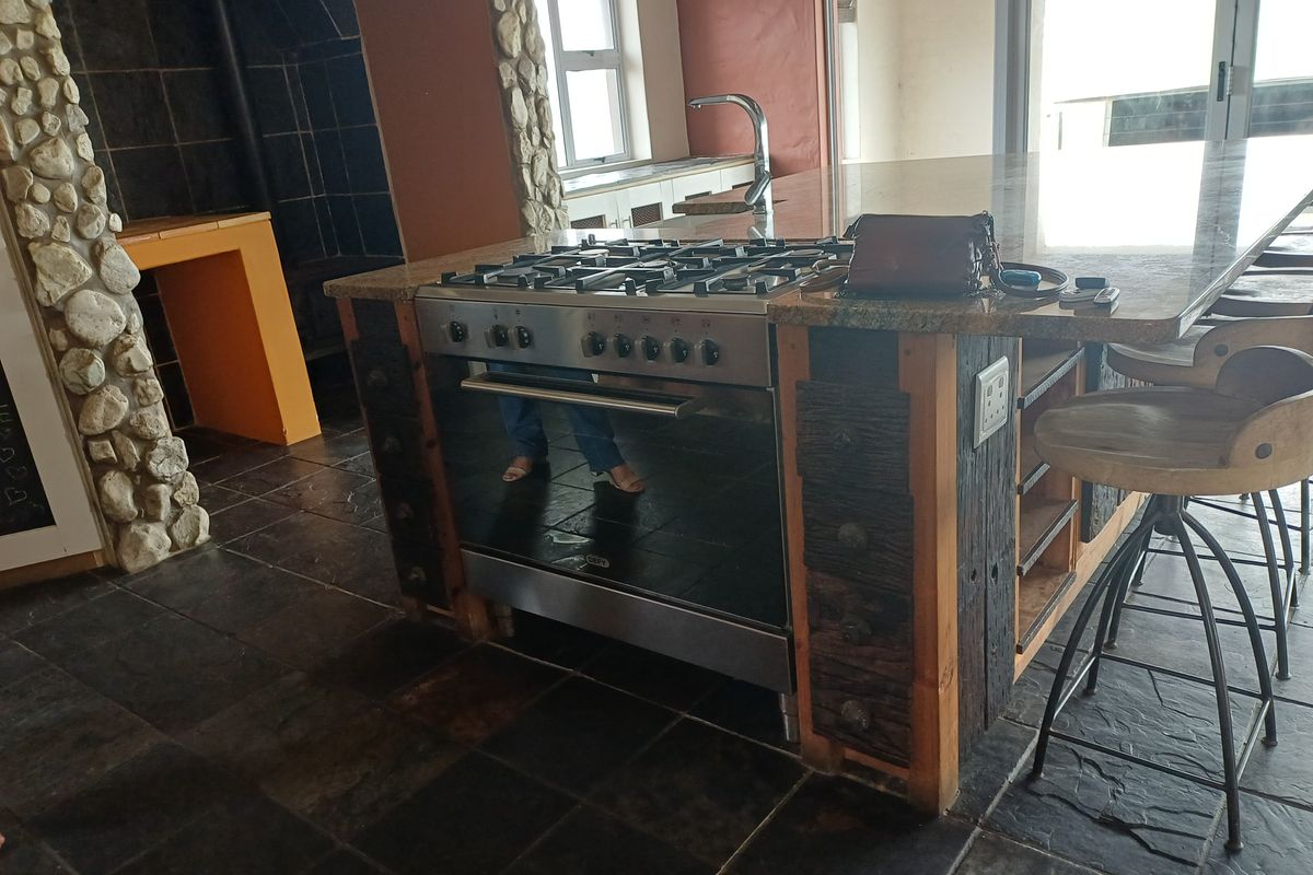 A rustic kitchen island featuring a built-in gas stove, granite countertop, and stone pillar accents, set against dark slate flooring.