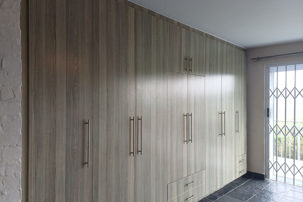 A spacious room featuring extensive floor-to-ceiling built-in cabinetry with wood-grain finish, complemented by dark slate tile flooring and a secure metal security gate.