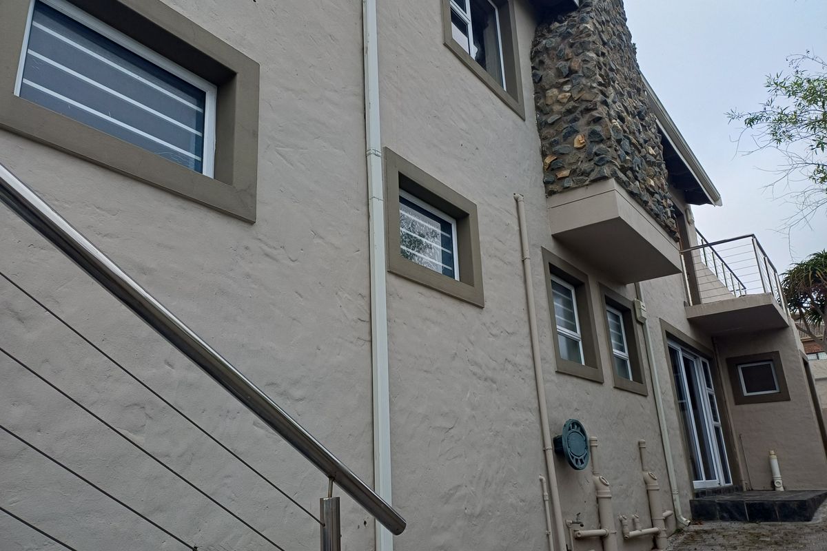 Side elevation of a multi-story residence featuring textured stucco walls, stone chimney cladding, stainless steel railings, and paved ground level access.