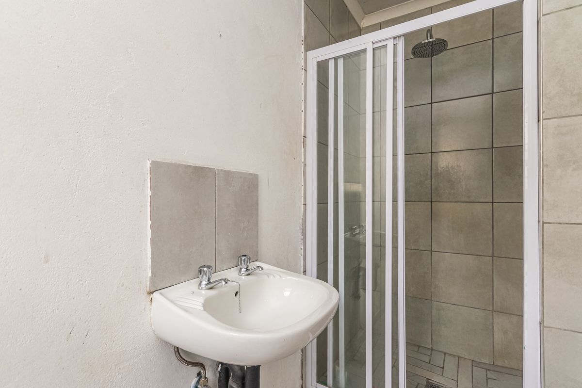 A compact bathroom featuring a wall-mounted basin and a shower enclosure with tiled walls and a rainfall showerhead.
