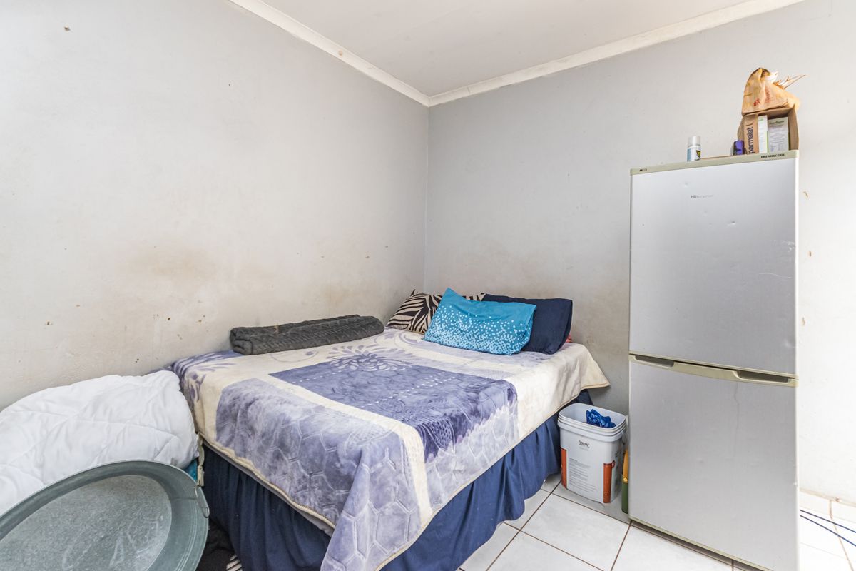 A compact bedroom featuring tiled flooring and plain wall finishes, currently utilized as a multi-purpose living space.