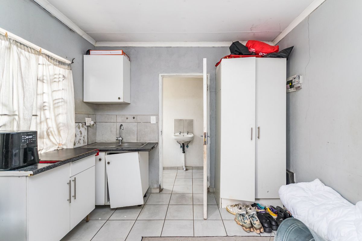 A small kitchen area featuring basic cabinetry, a sink, and tiled flooring, with an adjacent utility space visible through the doorway.