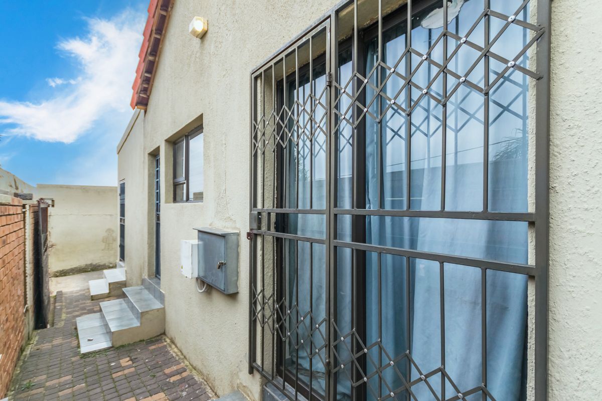 Side exterior view of the property featuring a paved walkway, security gates on sliding doors, and external utility housing.