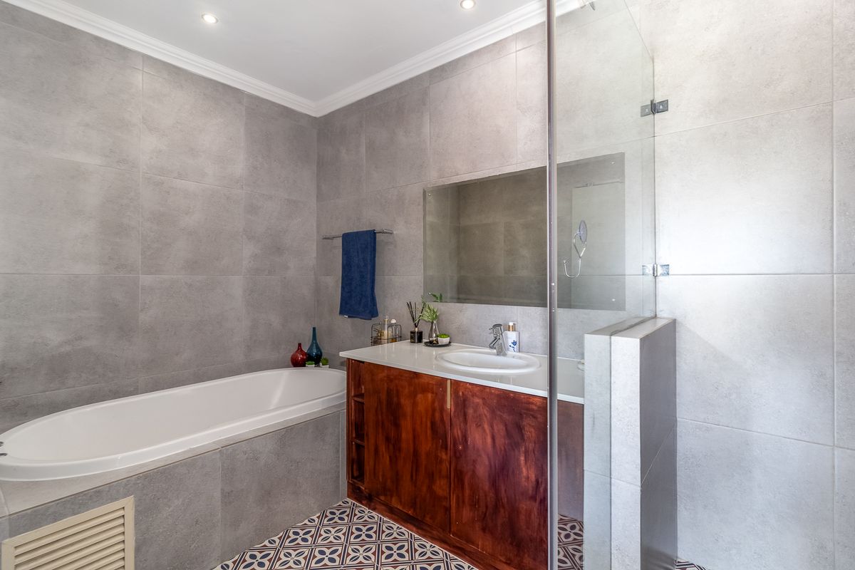 Modern bathroom featuring a built-in bathtub, a glass-enclosed shower, and a wooden vanity with a basin, complemented by grey wall tiles and patterned floor tiles.