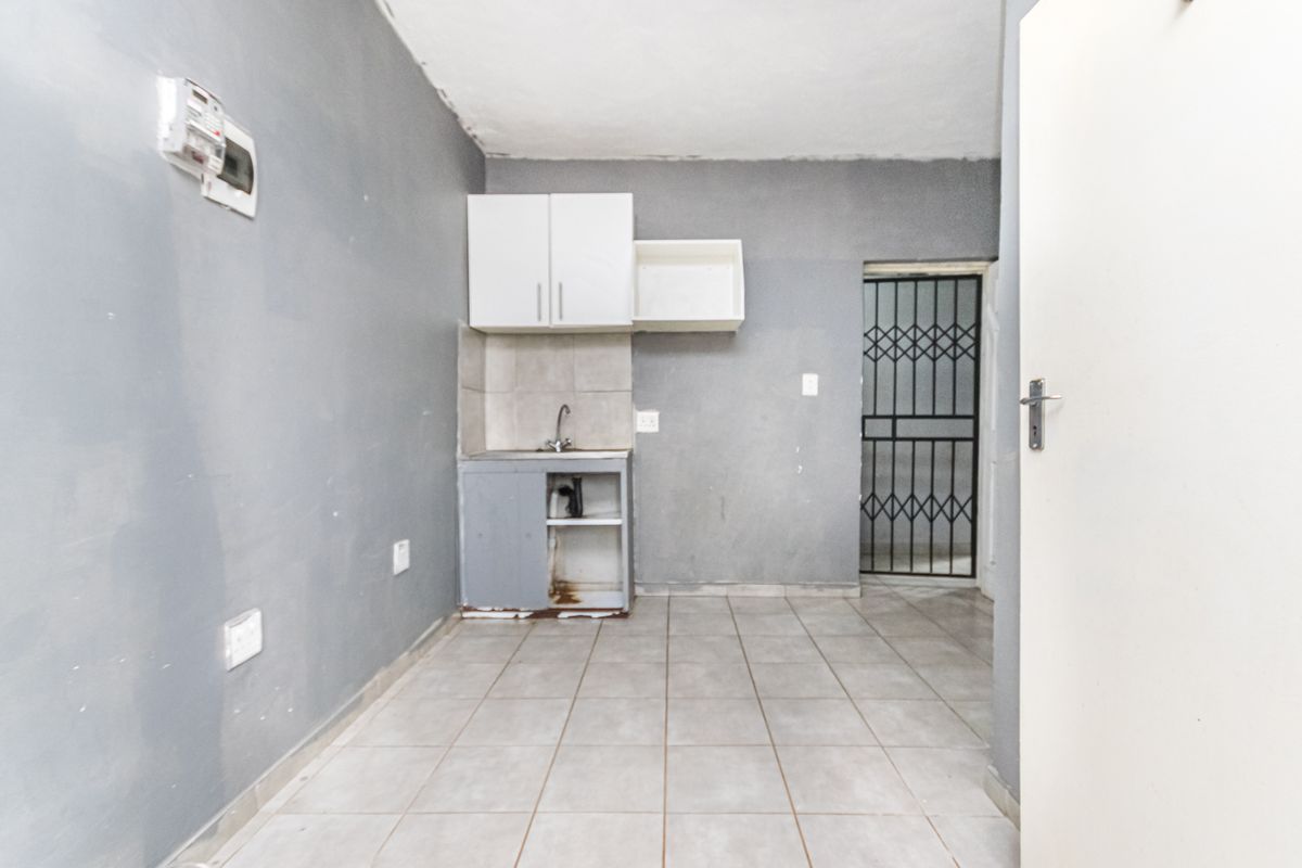 A small, basic kitchen area featuring tiled flooring, a single sink unit with overhead cabinetry, and a security gate leading to an exterior space.