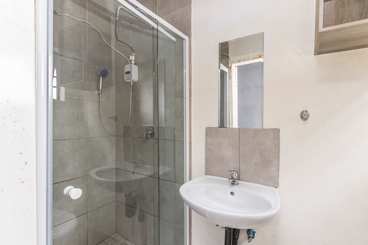 A compact bathroom featuring a glass-enclosed shower with wall-mounted electric shower unit and a wall-hung basin with a simple mirror.