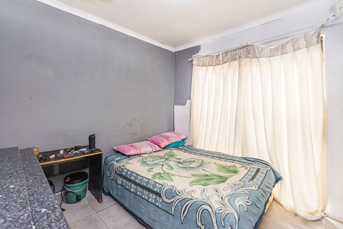A bedroom featuring tiled flooring and a large window with curtains. The room requires cosmetic updates to the wall finishes and ceiling.