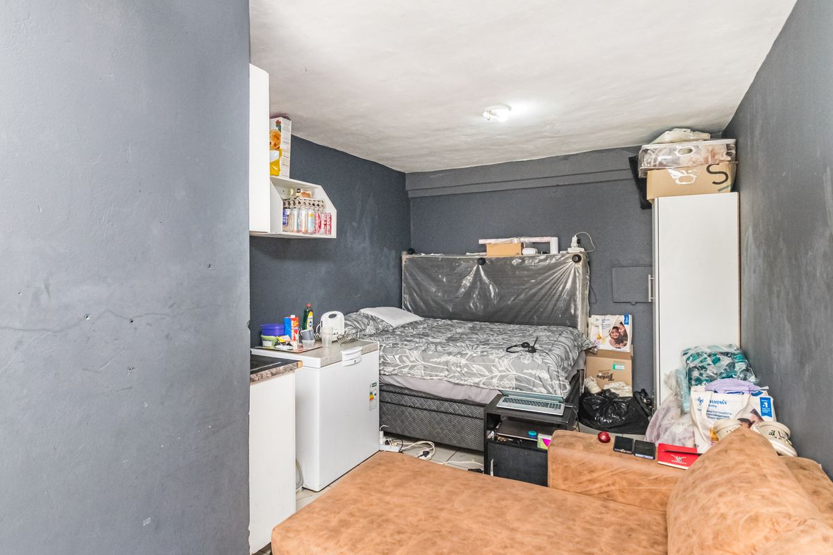 A compact studio-style bedroom featuring dark painted walls, tiled flooring, and a small kitchenette area with basic cabinetry.