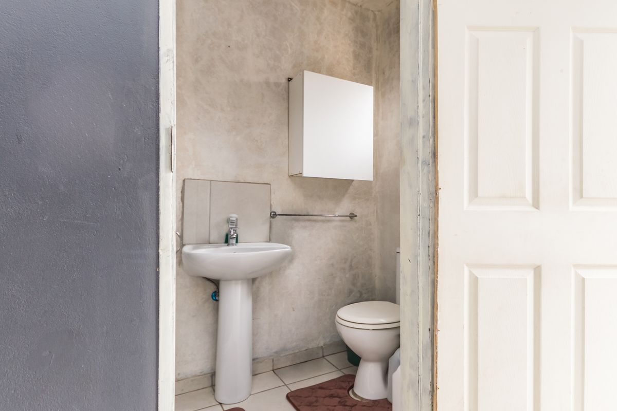 A compact guest bathroom featuring a pedestal basin, toilet, and wall-mounted cabinet with tiled flooring.