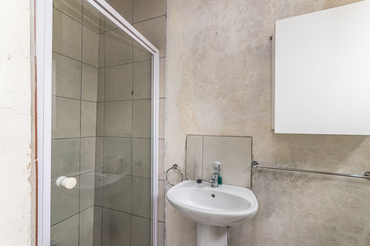 A compact bathroom featuring a pedestal basin, a shower enclosure with tiled walls, and a wall-mounted cabinet, requiring cosmetic updates to the wall finishes.