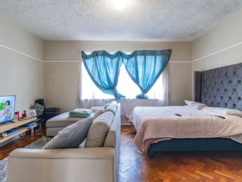 A bedroom featuring classic parquet flooring, a textured ceiling, and a picture rail, offering a functional space with potential for cosmetic updates.
