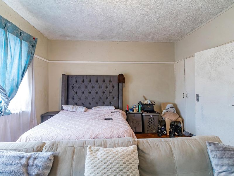 A bedroom featuring built-in cupboards and a textured ceiling, requiring cosmetic updates to the wall finishes and door surfaces.