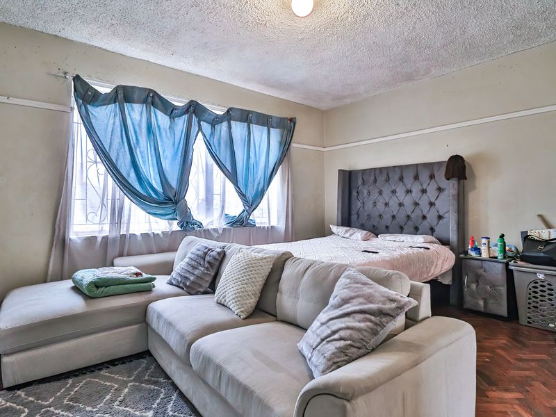 A bedroom featuring parquet flooring, a textured ceiling, and security bars on the window. The room requires cosmetic updates to improve its overall condition.