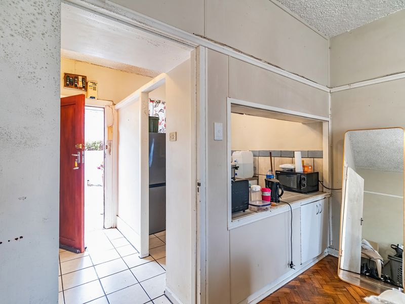 A dated kitchen area featuring a pass-through window, tiled and parquet flooring, requiring significant maintenance and cosmetic updates to improve its condition.