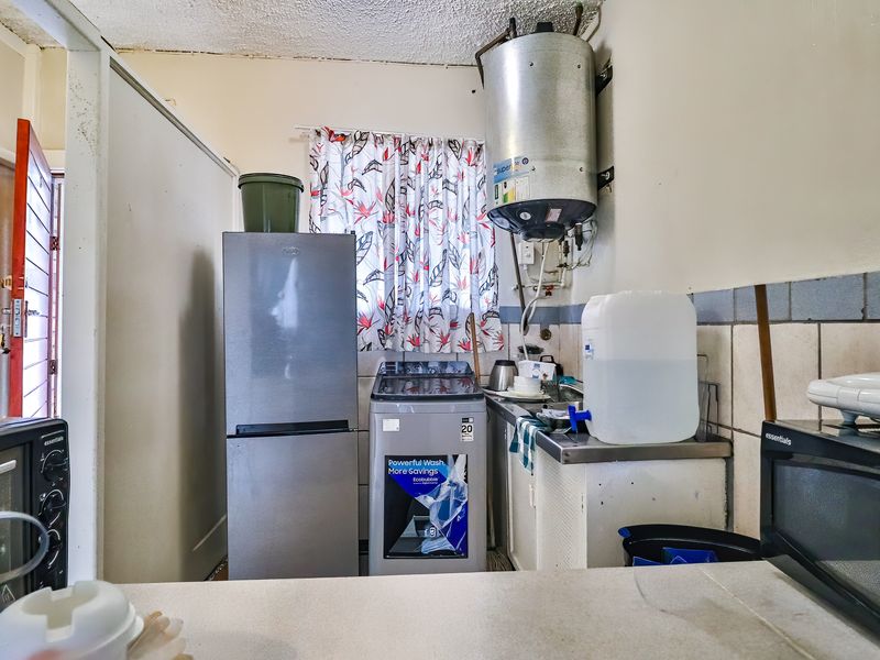 A functional laundry area featuring a wall-mounted electric geyser, tiled splashback, and built-in cabinetry with sink.
