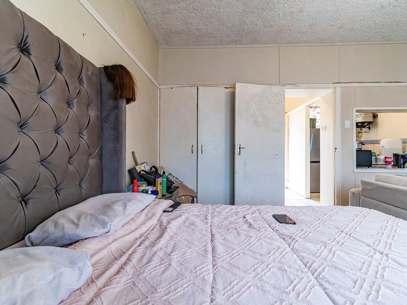 Bedroom featuring built-in cupboards and textured ceiling, with an adjacent view into the kitchen area.