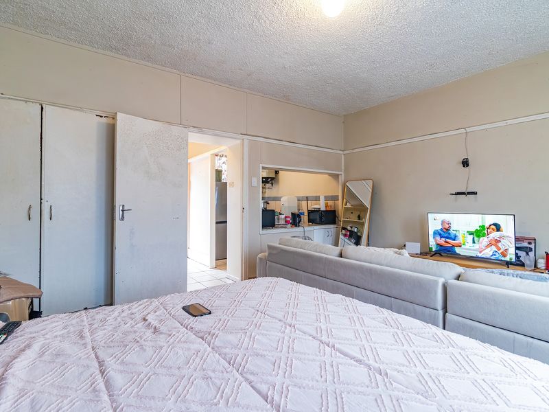 Bedroom featuring built-in cupboards and a pass-through window connecting to the kitchen area, showing signs of wear on the door and wall finishes.