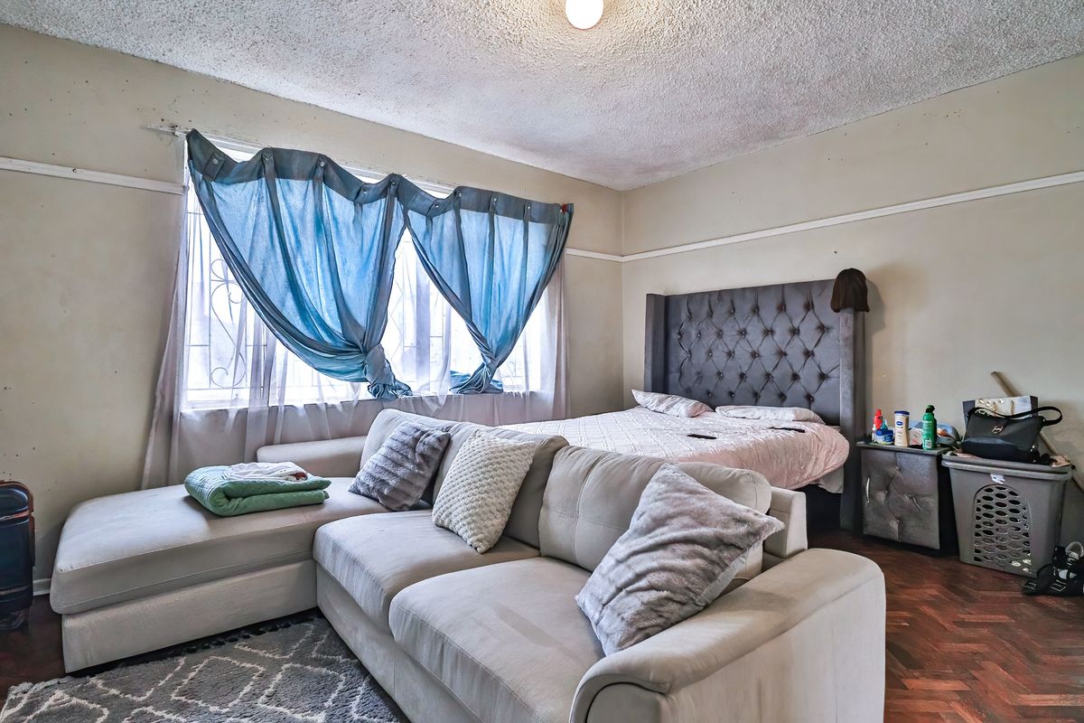 A bedroom featuring parquet flooring, a textured ceiling, and security bars on the window. The room requires cosmetic updates to improve its overall condition.