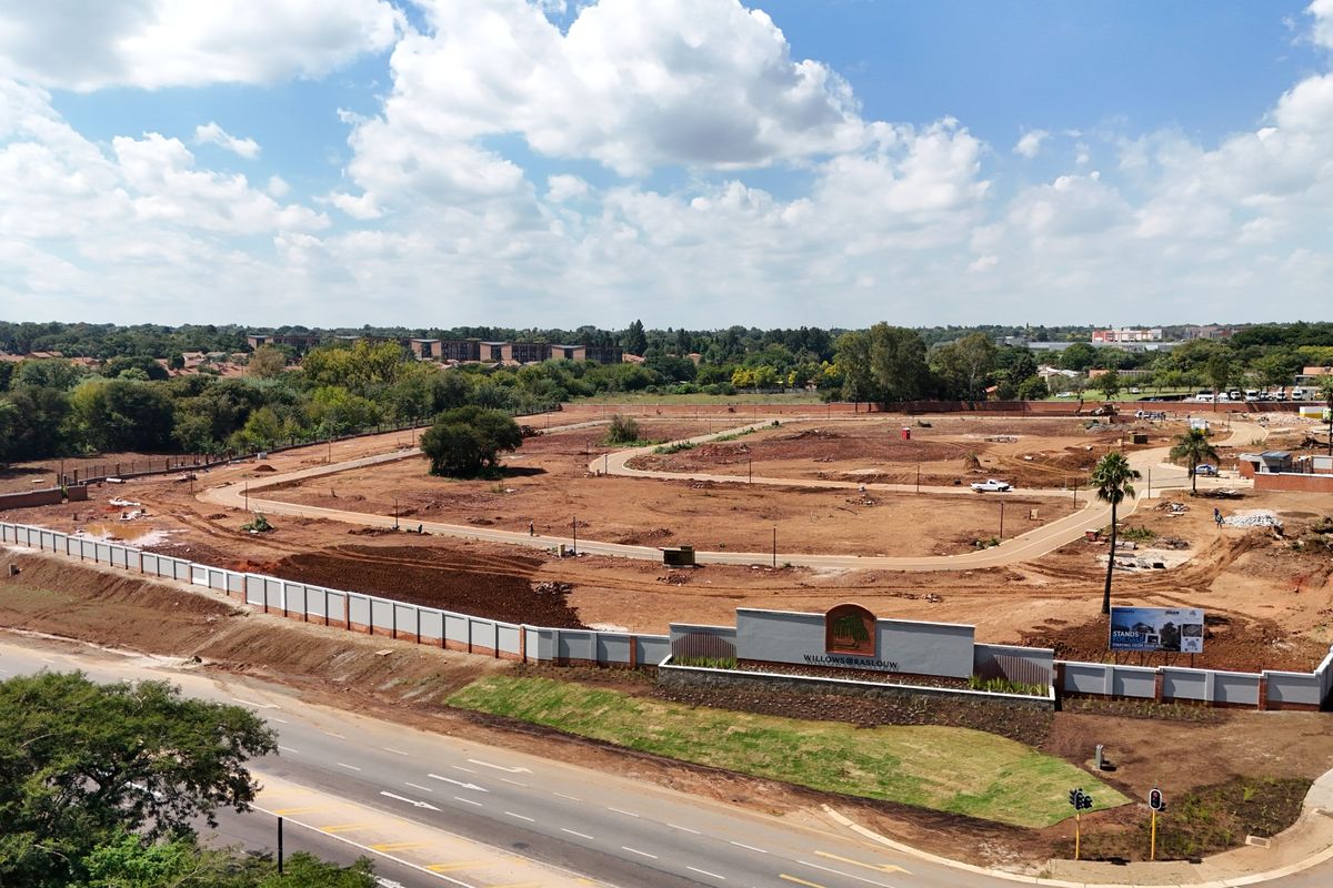 Aerial view of a residential development site featuring cleared land, perimeter walling, internal road infrastructure, and entrance signage.